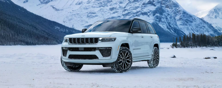 White 2026 Jeep Grand Cherokee parked in the snow, mountain in background.